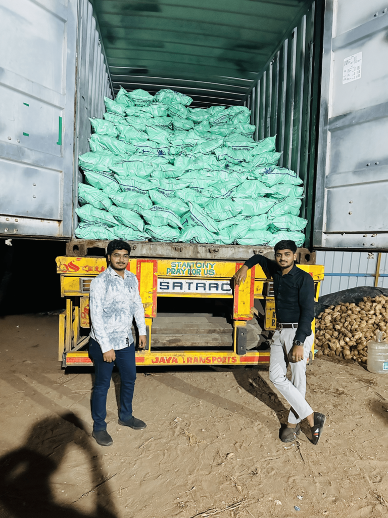 Two men standing in front of a loaded shipping container filled with green export bags, prepared for coconut transportation at a warehouse.